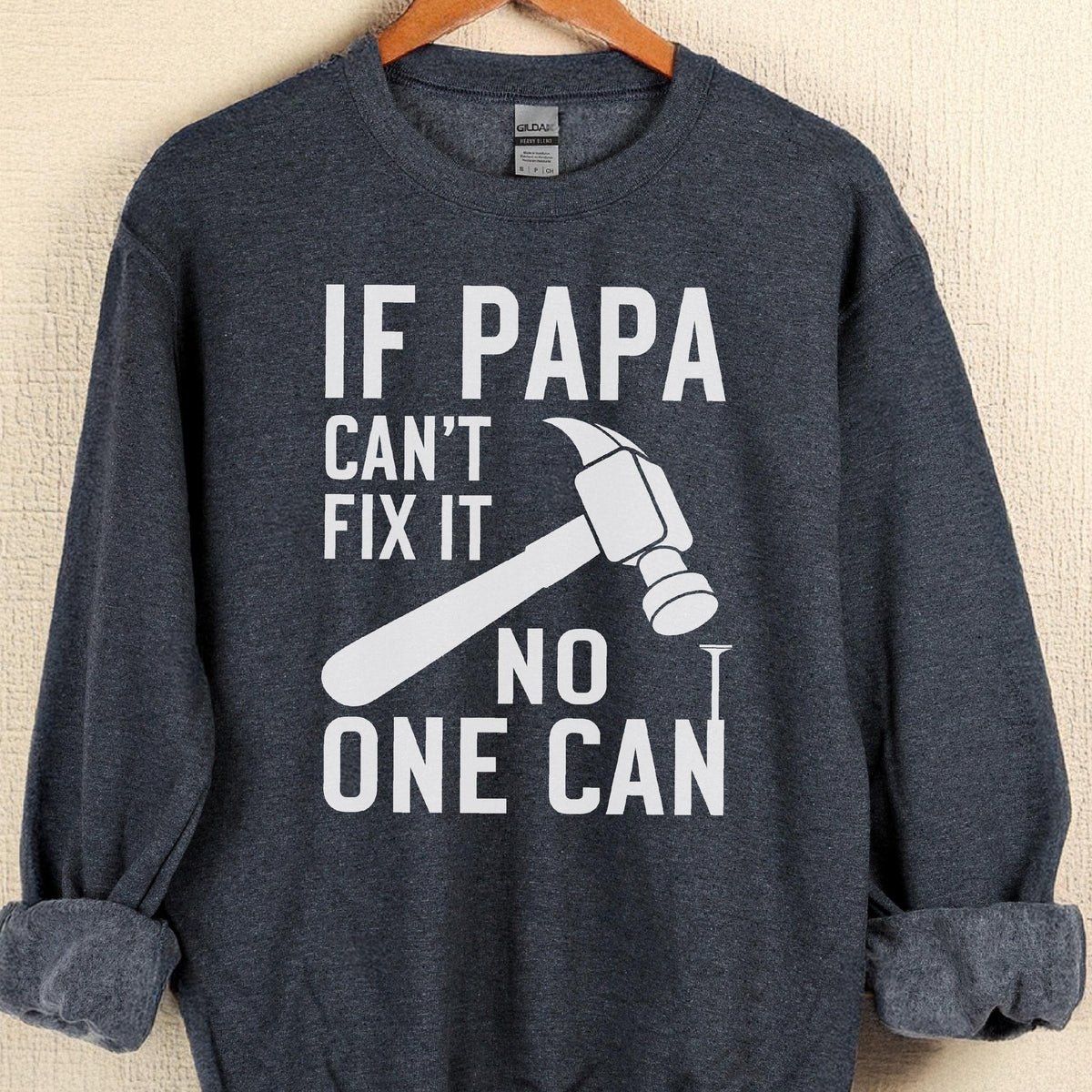 May include: A dark gray sweatshirt with the text "IF PAPA CAN'T FIX IT NO ONE CAN" in white. A white hammer and nail graphic are also featured on the front of the sweatshirt. The sweatshirt is hanging on a wooden hanger.