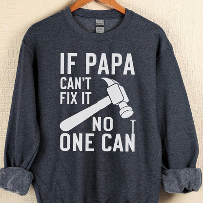 May include: A dark gray sweatshirt with the text "IF PAPA CAN'T FIX IT NO ONE CAN" in white. A white hammer and nail graphic are also featured on the front of the sweatshirt. The sweatshirt is hanging on a wooden hanger.
