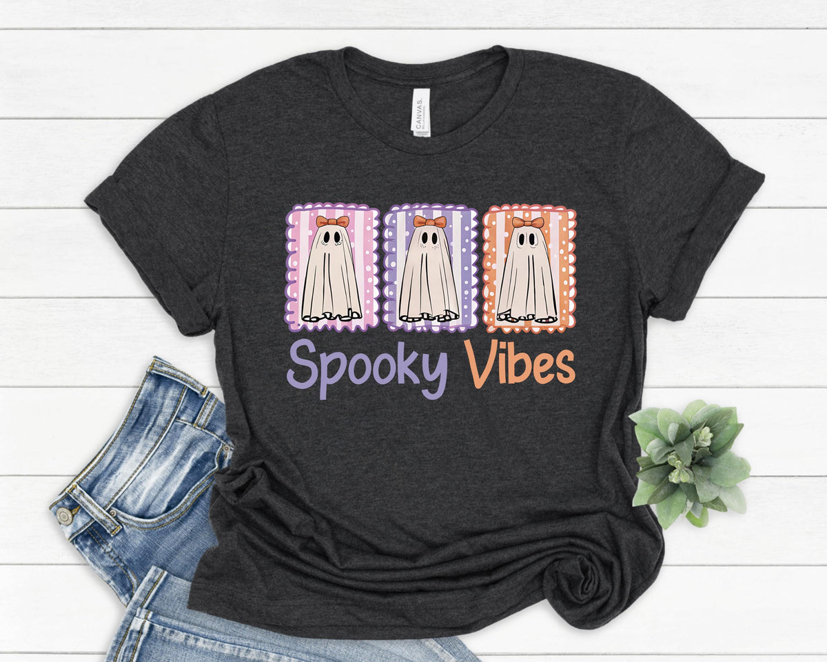 May include: Dark gray t-shirt with a Halloween-themed graphic. The design features three cartoon ghosts with bows in decorative frames, and the words "Spooky Vibes" in purple and orange.