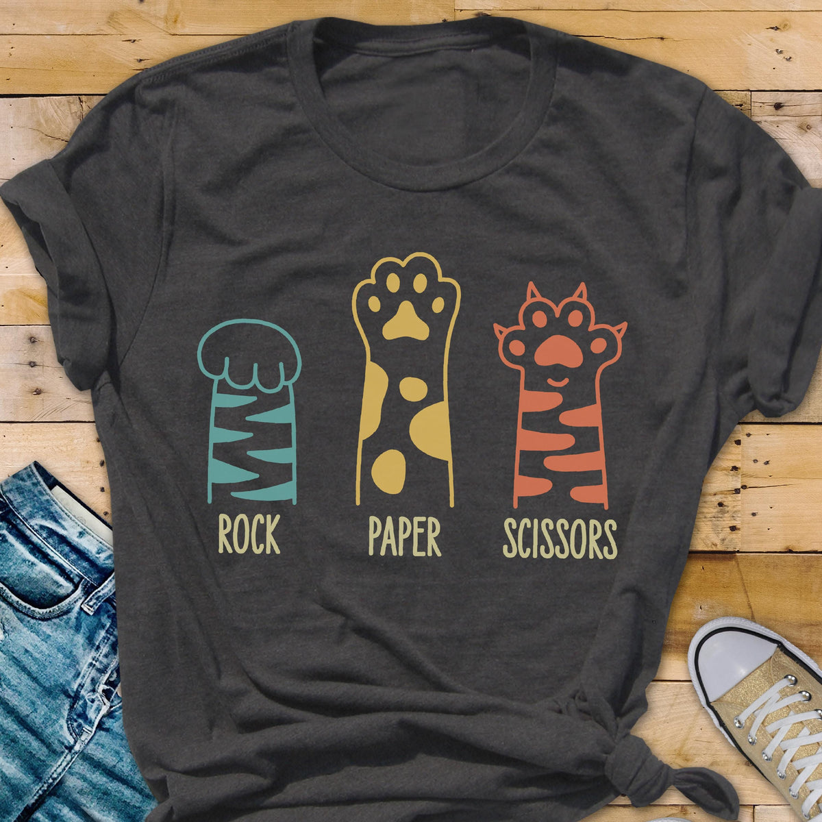 May include: A charcoal gray short-sleeve t-shirt featuring a graphic of three animal paws representing the game Rock, Paper, Scissors. The first paw is teal with stripes, the second is yellow with spots, and the third is orange with stripes.