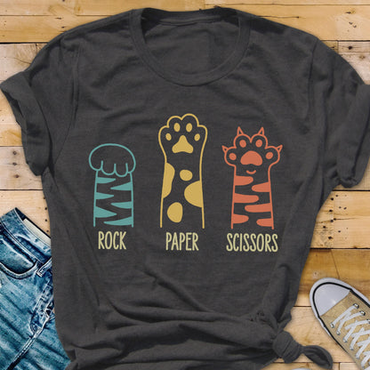 May include: A charcoal gray short-sleeve t-shirt featuring a graphic of three animal paws representing the game Rock, Paper, Scissors. The first paw is teal with stripes, the second is yellow with spots, and the third is orange with stripes.