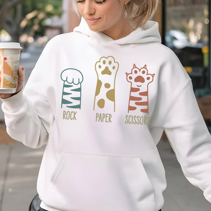 May include: A white hooded sweatshirt featuring a graphic of three cat paws with the text ROCK, PAPER, SCISSORS printed below them. The first paw is blue-striped, the second is gold-spotted, and the third is orange-striped with extended claws.