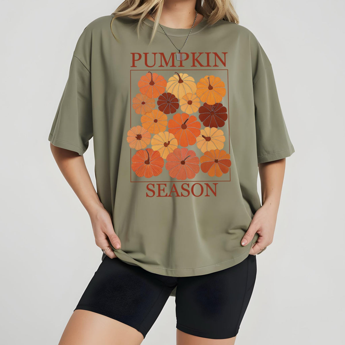 May include: Olive green t-shirt with a rectangular graphic featuring various orange and brown pumpkins. The words "PUMPKIN SEASON" are printed above and below the pumpkins in a reddish-brown color.