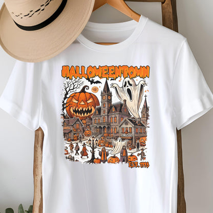 May include: White t-shirt featuring a Halloween-themed graphic. The design includes a jack-o'-lantern, a haunted house, ghosts, and the text "Halloweentown" in orange. The shirt also has the text "EST. 1998".
