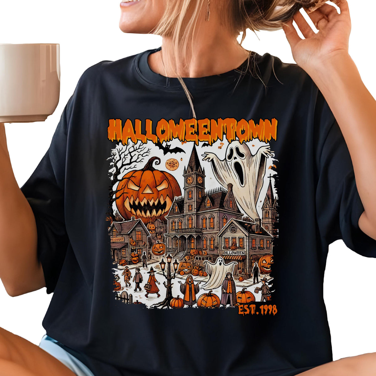 May include: A black t-shirt featuring a graphic print with the text HALLOWEENTOWN and EST. 1998. The design displays a large jack-o'-lantern, a haunted clock tower building, ghosts, and various figures in a town setting with orange and black colors.