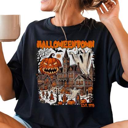 May include: A black t-shirt featuring a graphic print with the text HALLOWEENTOWN and EST. 1998. The design displays a large jack-o'-lantern, a haunted clock tower building, ghosts, and various figures in a town setting with orange and black colors.