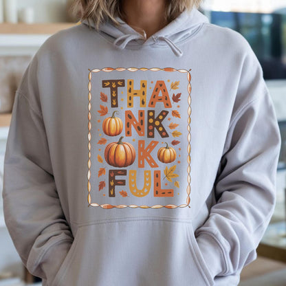 May include: A light gray hoodie with a graphic that says "THANKFUL" in brown, orange, and yellow letters. The design includes pumpkins and fall leaves within a decorative border, perfect for Thanksgiving.