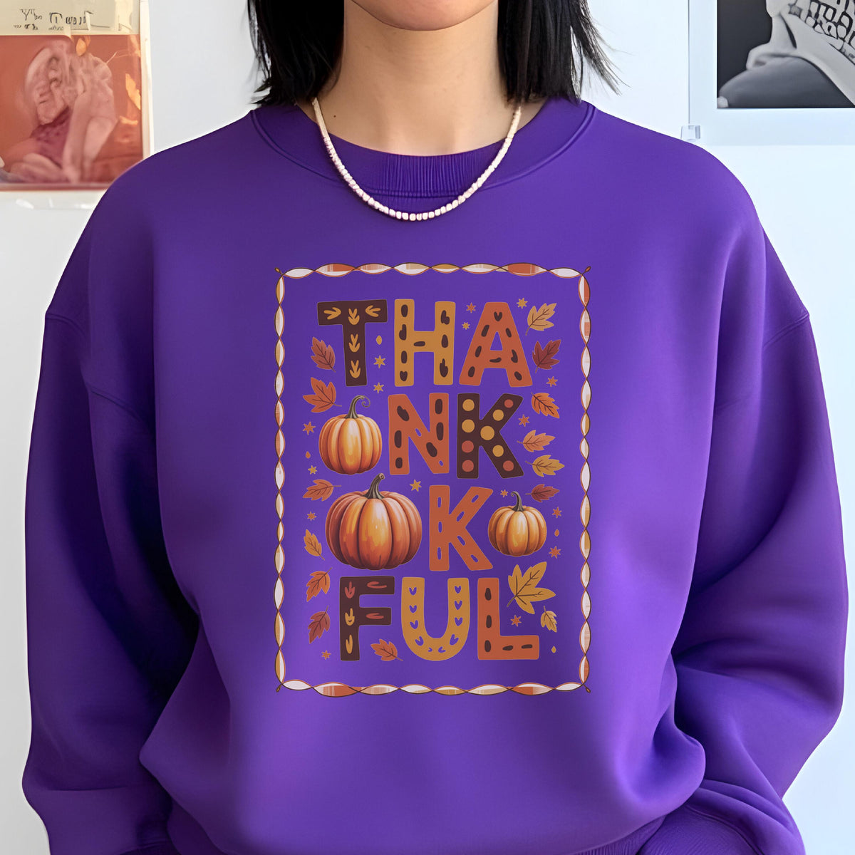 May include: A purple sweatshirt with the word "THANKFUL" in a fall-themed design. The design includes pumpkins and autumn leaves in shades of orange, brown, and yellow. The sweatshirt is a solid purple color.
