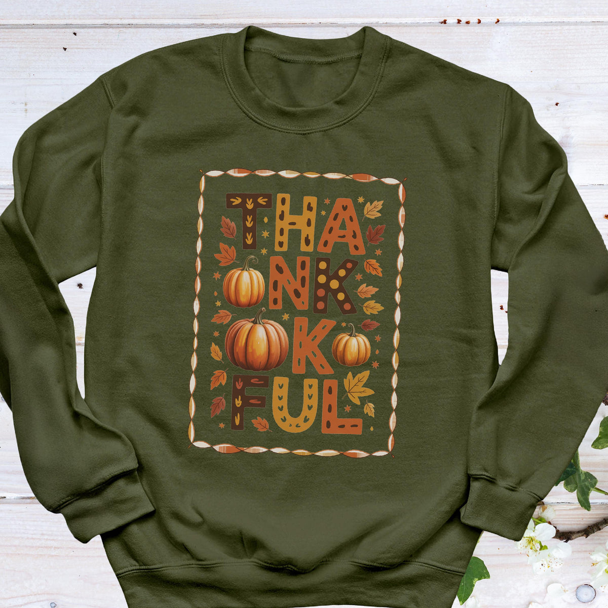 May include: An olive green sweatshirt with the word "THANKFUL" in a fall-themed design. The word is in orange and brown with pumpkins and leaves. The sweatshirt is a long-sleeved crew neck.