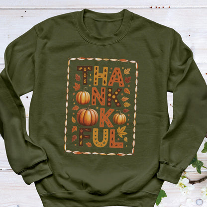 May include: An olive green sweatshirt with the word "THANKFUL" in a fall-themed design. The word is in orange and brown with pumpkins and leaves. The sweatshirt is a long-sleeved crew neck.