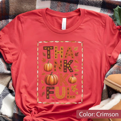 May include: Crimson-colored t-shirt with the word "THANKFUL" in a decorative design. The design includes pumpkins and fall leaves. The shirt is made of a soft material and is perfect for the autumn season.