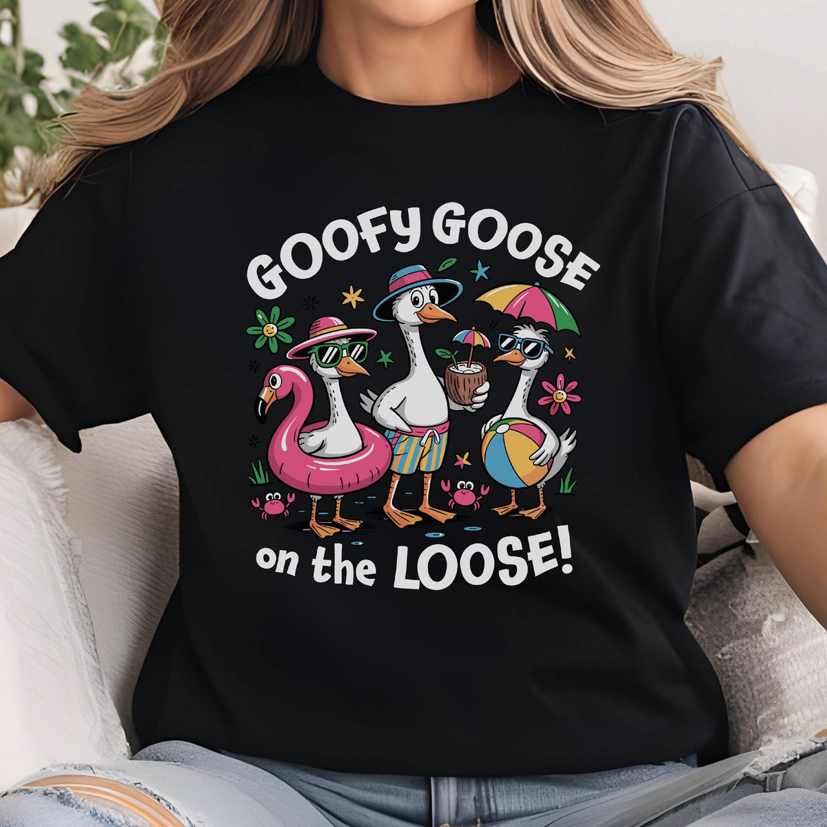 May include: Black t-shirt featuring a whimsical graphic of three geese enjoying a beach day. The geese are wearing sunglasses, hats, and holding beach accessories. The text "GOOFY GOOSE on the LOOSE!" is printed above and below the geese.