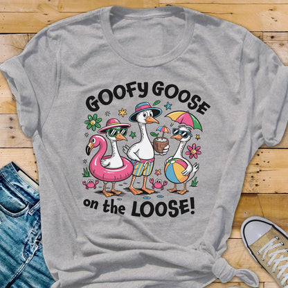 May include: A gray t-shirt featuring a cartoon illustration of three geese on vacation. The geese are wearing sunglasses, hats, and swim trunks, with one riding a pink flamingo float. The text "GOOFY GOOSE on the LOOSE!" is printed on the shirt.