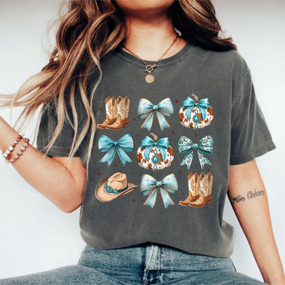 May include: Dark gray t-shirt featuring a collage of cowboy boots, bows, pumpkins, and a cowboy hat. The design includes light blue bows and pumpkins with a cowhide pattern. The shirt has a relaxed fit.