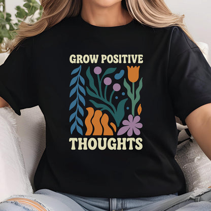 May include: Black t-shirt with the words "GROW POSITIVE THOUGHTS" in a cream color. The shirt features a colorful floral design with blue, orange, purple, and green elements. The design has a retro, vintage aesthetic.