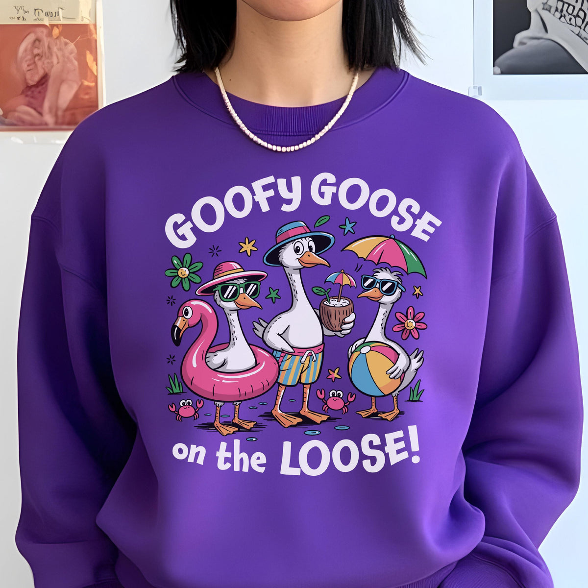 May include: A purple sweatshirt with the phrase "GOOFY GOOSE on the LOOSE!" and a graphic of three cartoon geese in sunglasses and beach attire. One goose is in a flamingo float, another holds a coconut drink, and the third has a beach ball.