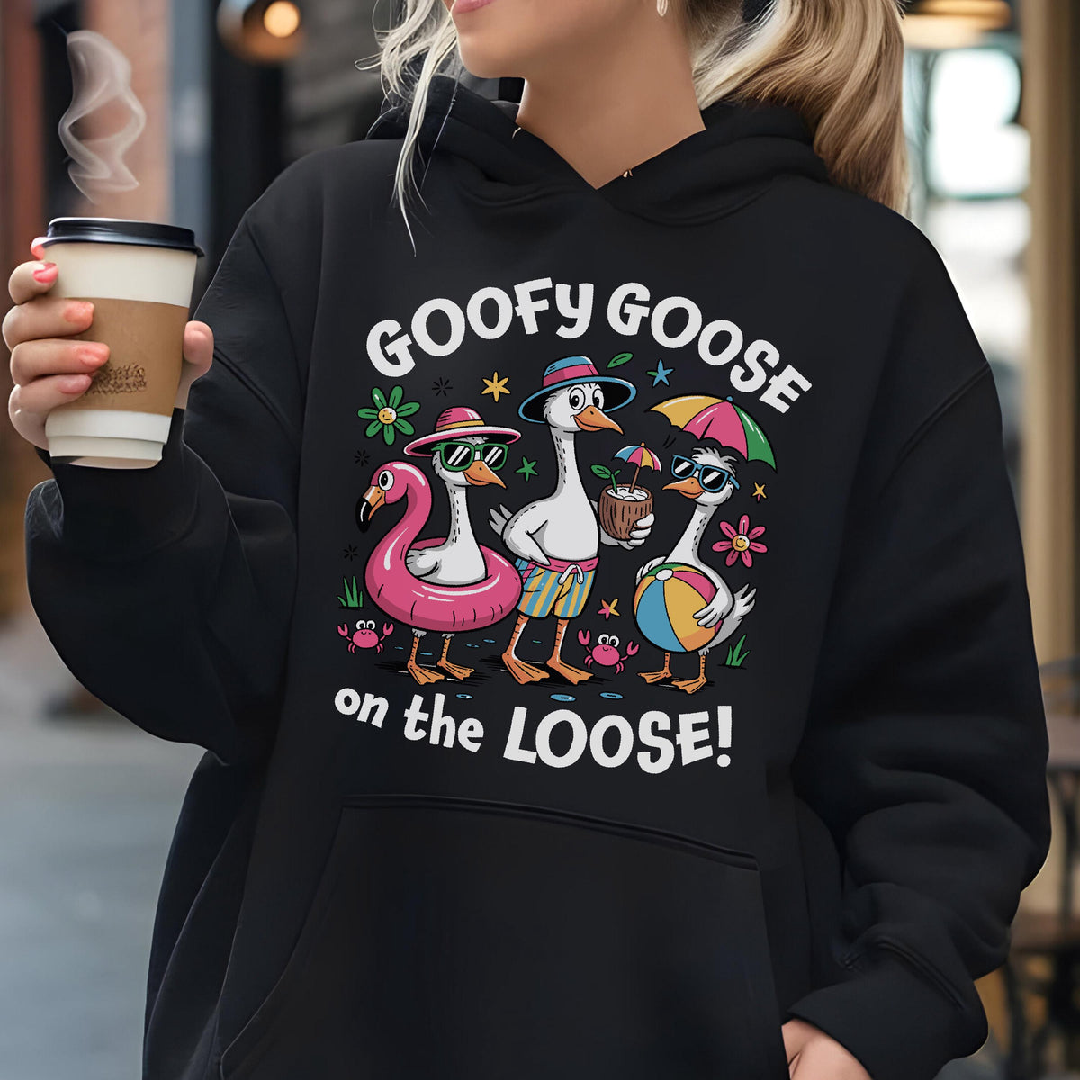 May include: Black hoodie featuring a cartoon design of three geese in sunglasses and beach attire. The text "GOOFY GOOSE on the LOOSE!" is printed above the geese. The geese are wearing a flamingo float, holding a coconut drink, and a beach ball.