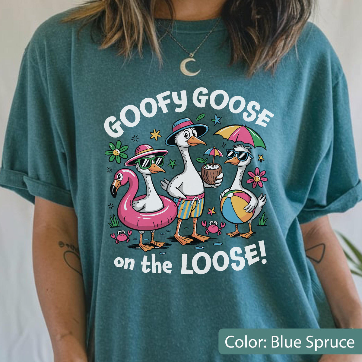 May include: A blue spruce t-shirt featuring a graphic of three geese with the text GOOFY GOOSE on the LOOSE! The geese are depicted with summer accessories including a pink flamingo pool float, sunglasses, a coconut drink, and a beach ball.