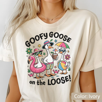 May include: An ivory t-shirt featuring a graphic of three geese on vacation. The text reads GOOFY GOOSE on the LOOSE! The geese wear hats and sunglasses, with one in a pink flamingo floatie, one holding a coconut drink, and one holding a beach ball.