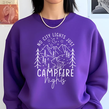 May include: A vibrant purple crewneck sweatshirt featuring a white graphic print of a mountain landscape, pine trees, a winding river, a campfire, and a crescent moon with stars. The text reads NO CITY LIGHTS JUST CAMPFIRE Nights in white.