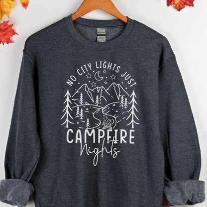 May include: A dark charcoal gray crewneck sweatshirt featuring a white graphic print of mountains, pine trees, a crescent moon, stars, and a campfire. The text reads "NO CITY LIGHTS JUST CAMPFIRE NIGHTS" in a mix of block and script lettering.