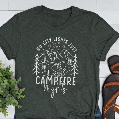 May include: A dark heather gray short-sleeve t-shirt featuring a white graphic print of mountains, pine trees, a crescent moon, stars, and a campfire. The text reads NO CITY LIGHTS JUST CAMPFIRE Nights in a mix of block and script lettering.