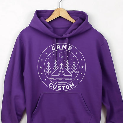 May include: A vibrant purple hooded sweatshirt featuring a white circular graphic on the chest. The design depicts a tent, pine trees, a crescent moon, and stars, with the text CAMP CUSTOM printed in a circular border around the central illustration.