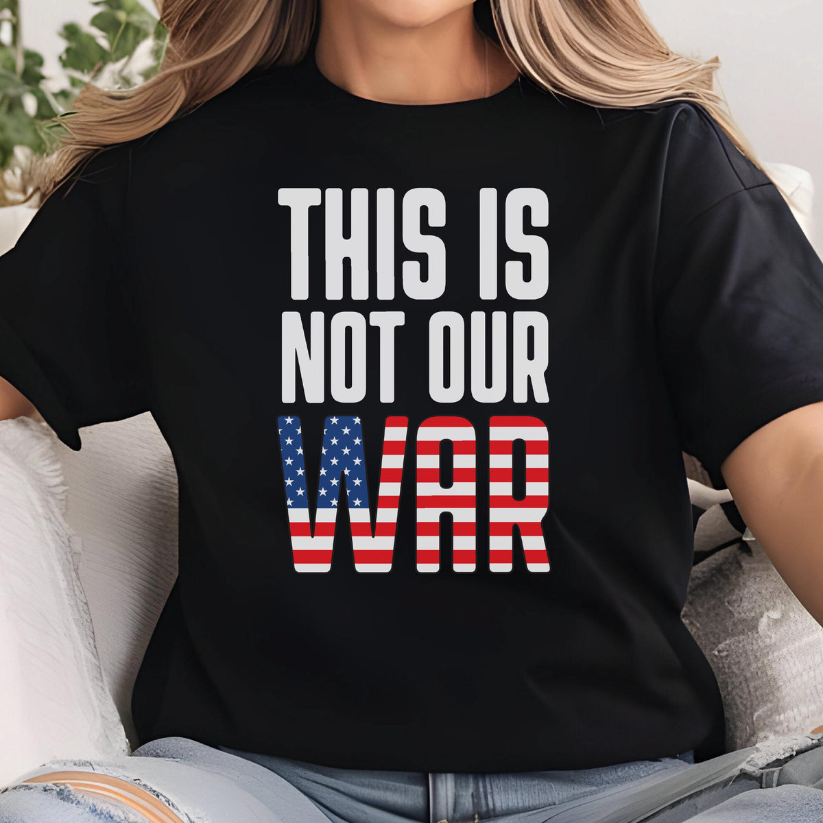 May include: Black t-shirt with the text "THIS IS NOT OUR WAR" in white. The word "WAR" is designed with the American flag's stars and stripes. The shirt is a casual wear item.