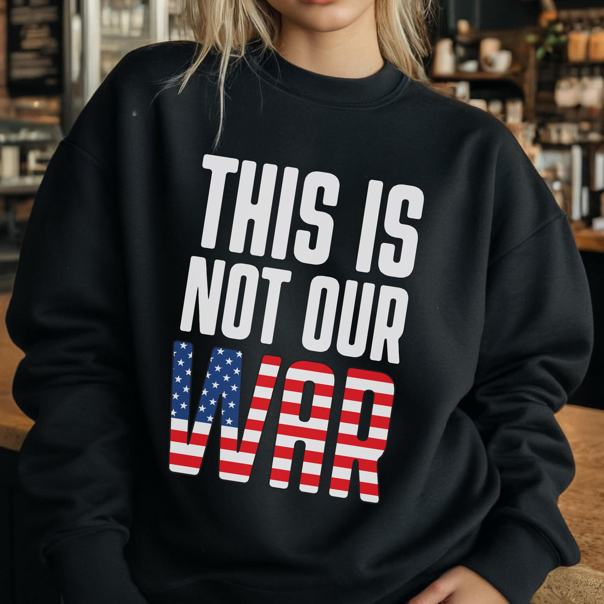 May include: Black sweatshirt with the text "THIS IS NOT OUR WAR" in white block letters. The word "WAR" is designed with the American flag's stars and stripes.