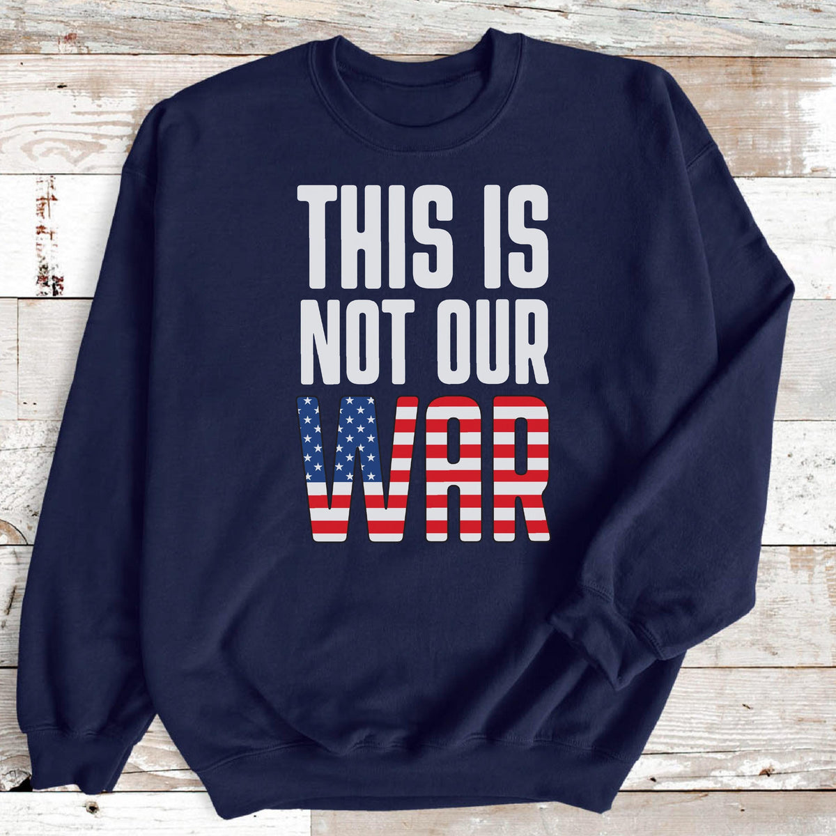 May include: Navy blue sweatshirt with the text "THIS IS NOT OUR WAR" in white block letters. The word "WAR" is designed with the American flag's stars and stripes.