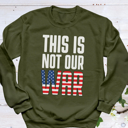 May include: An olive green sweatshirt with the text "THIS IS NOT OUR WAR" in white block letters. The word "WAR" is designed with the American flag's stars and stripes.