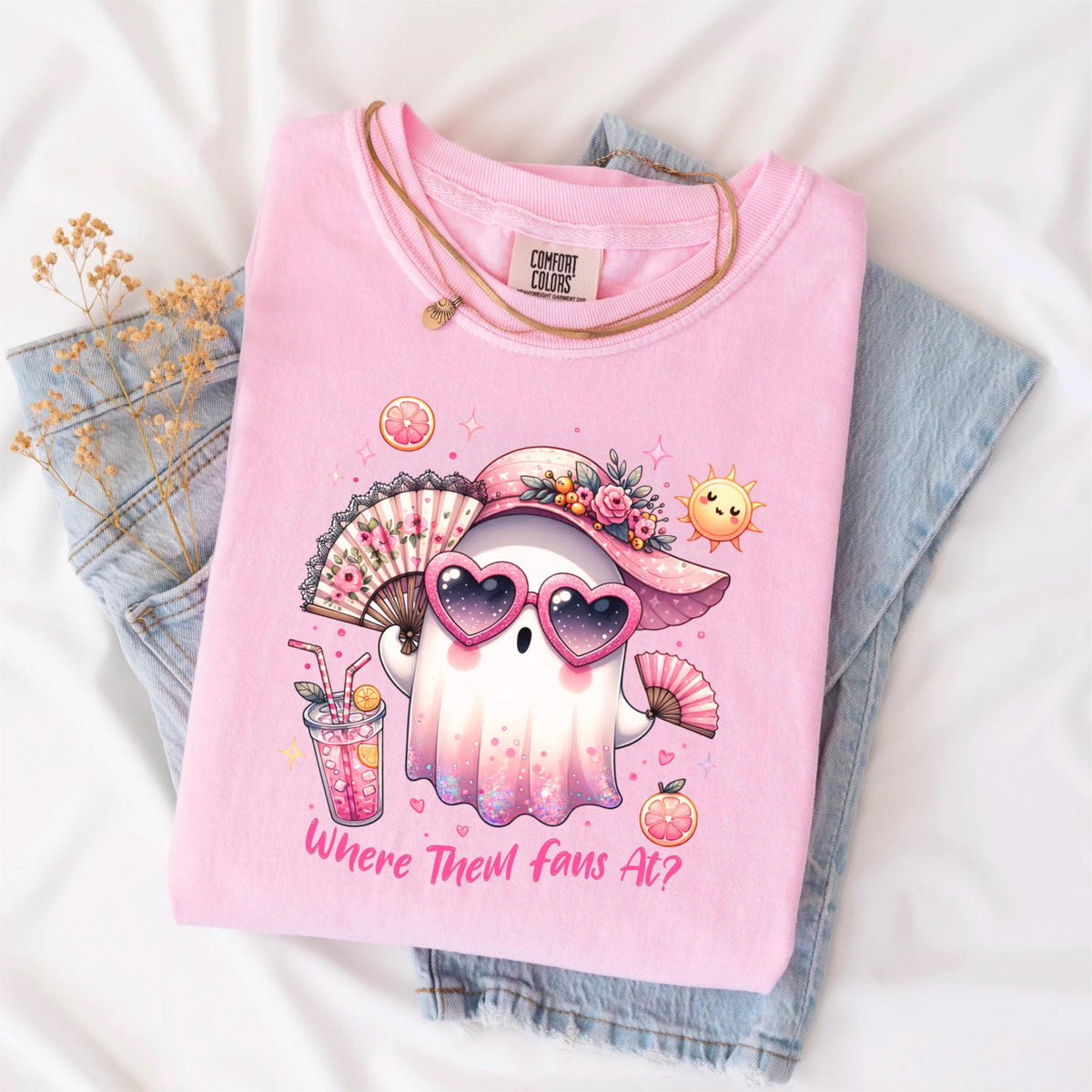 May include: Pink Comfort Colors t-shirt with a graphic of a ghost wearing heart-shaped sunglasses and a sun hat, holding a fan and a drink. The text "Where Them Fans At?" is printed on the shirt. A gold necklace and folded blue jeans are also in the image.