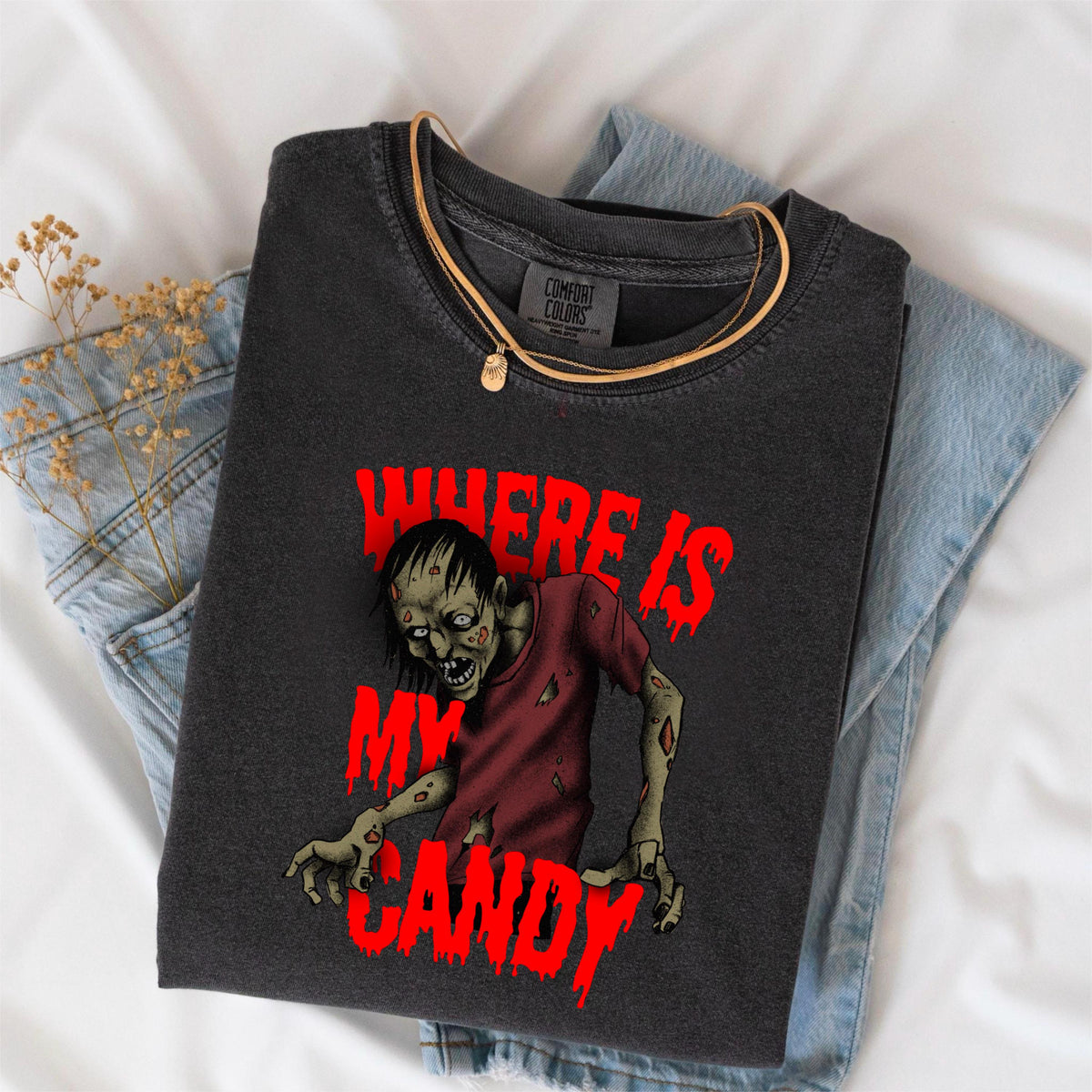 May include: Dark gray t-shirt with a zombie graphic and the text "WHERE IS MY CANDY" in red. The shirt is folded on top of blue jeans and a gold necklace.