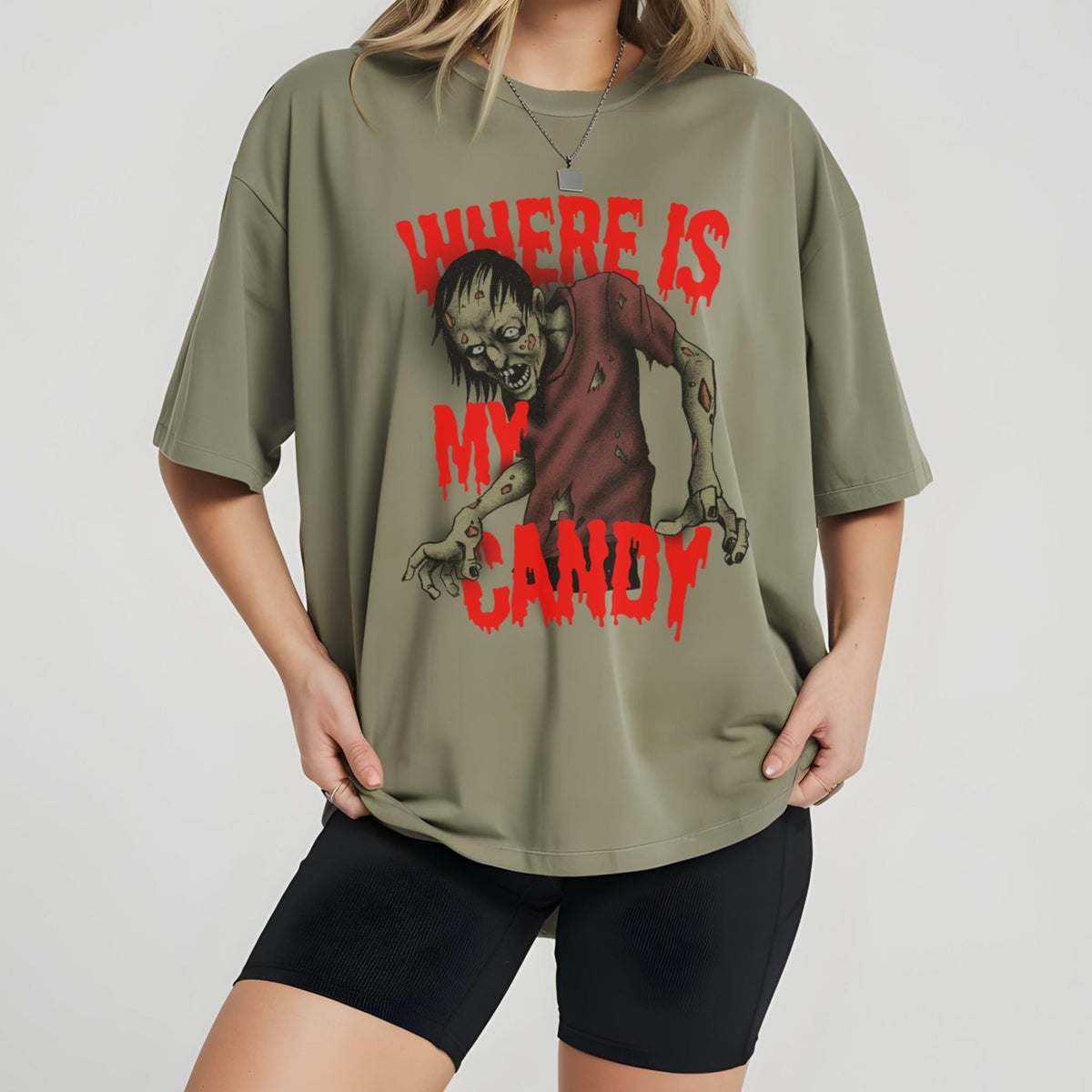 May include: Olive green t-shirt featuring a zombie graphic with the text "WHERE IS MY CANDY" in red. The zombie is depicted in a distressed style, with a red shirt and exposed flesh. The shirt has short sleeves and a relaxed fit.