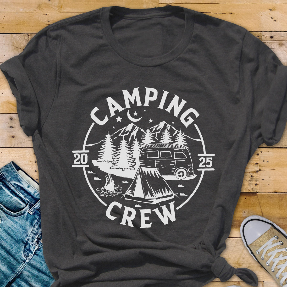 May include: A dark gray short-sleeve t-shirt featuring a white circular graphic. The design includes a camper van, a tent, a campfire, pine trees, mountains, stars, and a crescent moon. The text reads CAMPING CREW with the numbers 20 and 25.