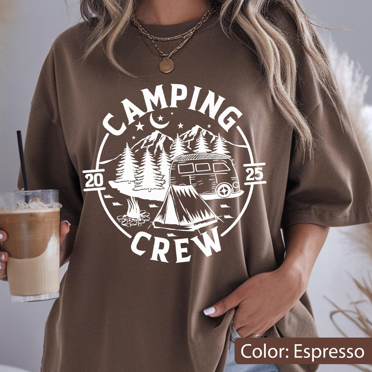May include: An espresso brown short-sleeve t-shirt featuring a white circular graphic print. The design includes a camper van, a tent, a campfire, pine trees, mountains, stars, and a crescent moon, with the text "CAMPING CREW 2025" printed around it.