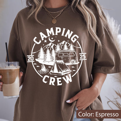 May include: An espresso brown short-sleeve t-shirt featuring a white circular graphic print. The design includes a camper van, a tent, a campfire, pine trees, mountains, stars, and a crescent moon, with the text "CAMPING CREW 2025" printed around it.