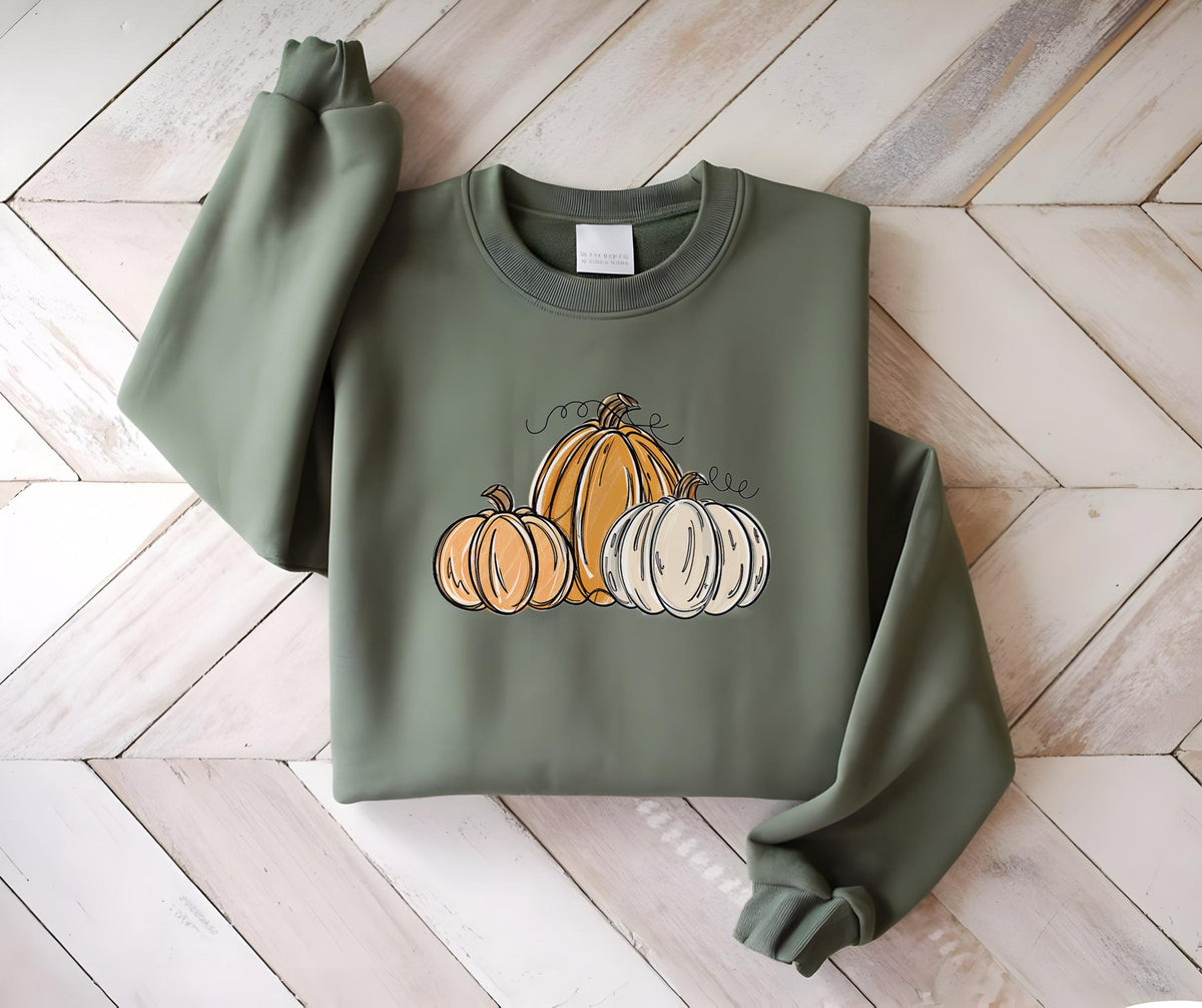 May include: Olive green sweatshirt featuring a pumpkin graphic. The graphic includes three pumpkins in shades of orange and white with black line art details. The sweatshirt has a crew neck and long sleeves.