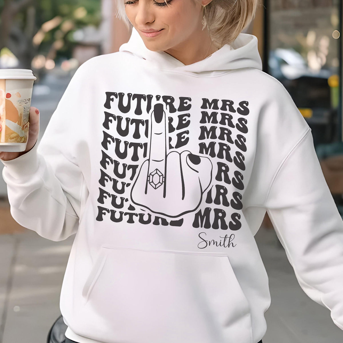 May include: White hoodie with a black graphic of a hand giving the middle finger, wearing a diamond ring. The words "FUTURE MRS" are printed around the hand. The name "Smith" is printed below the hand.