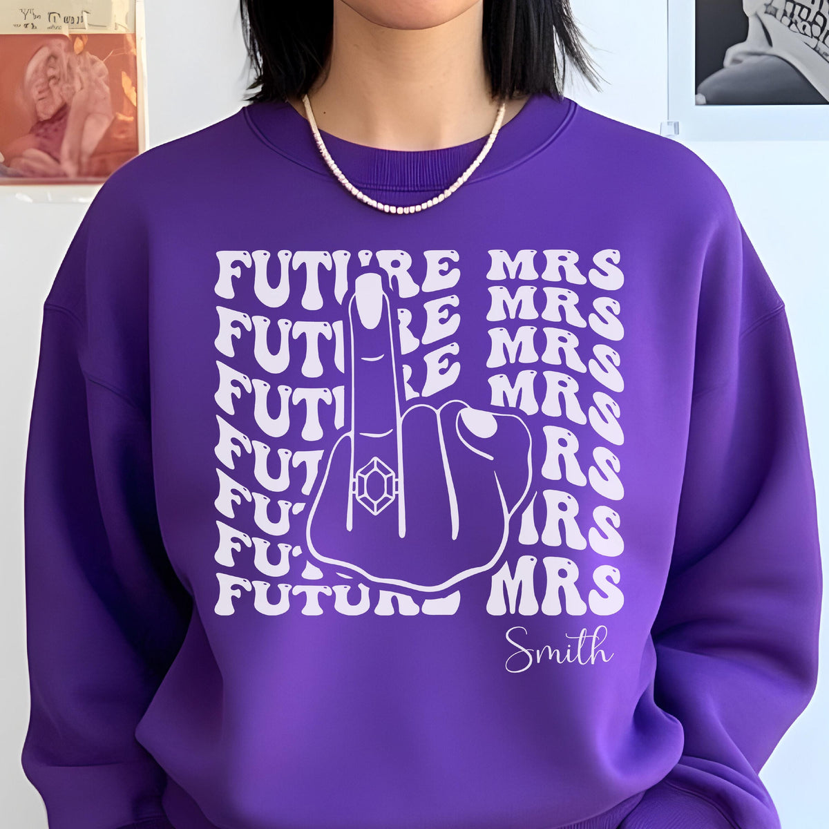 May include: A purple sweatshirt with the text "FUTURE MRS" repeated in a stacked pattern, with a graphic of a hand giving the middle finger, wearing a ring. The name "Smith" is written below the graphic.