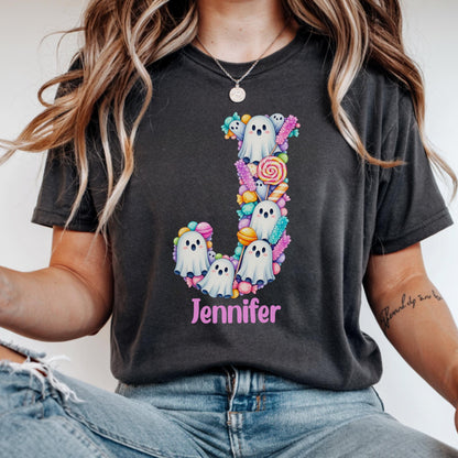 May include: A charcoal gray t-shirt featuring a large letter J composed of white ghost illustrations and colorful candy graphics, including lollipops and rock candy. The name Jennifer is printed in pink text below the letter J graphic.