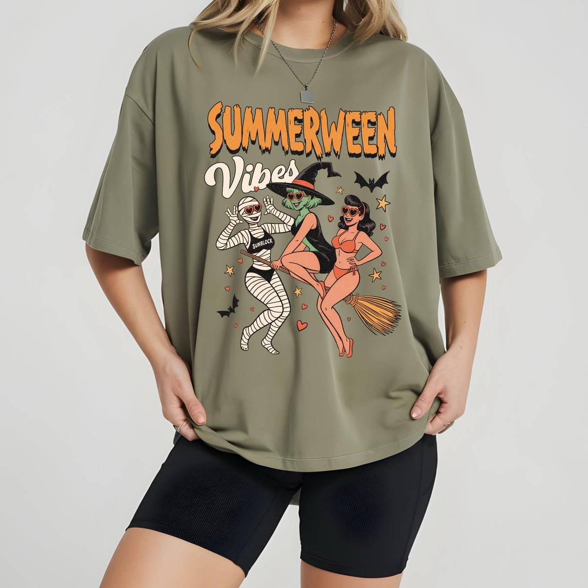 May include: Olive green t-shirt with the words "Summerween Vibes" in orange and white. The graphic features three cartoon characters: a mummy, a witch, and a woman in a swimsuit, with bats and stars.