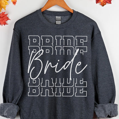 May include: A dark charcoal gray crewneck sweatshirt featuring the word Bride printed in a white script font layered over the word BRIDE repeated in a white block letter varsity style font across the center of the chest area.