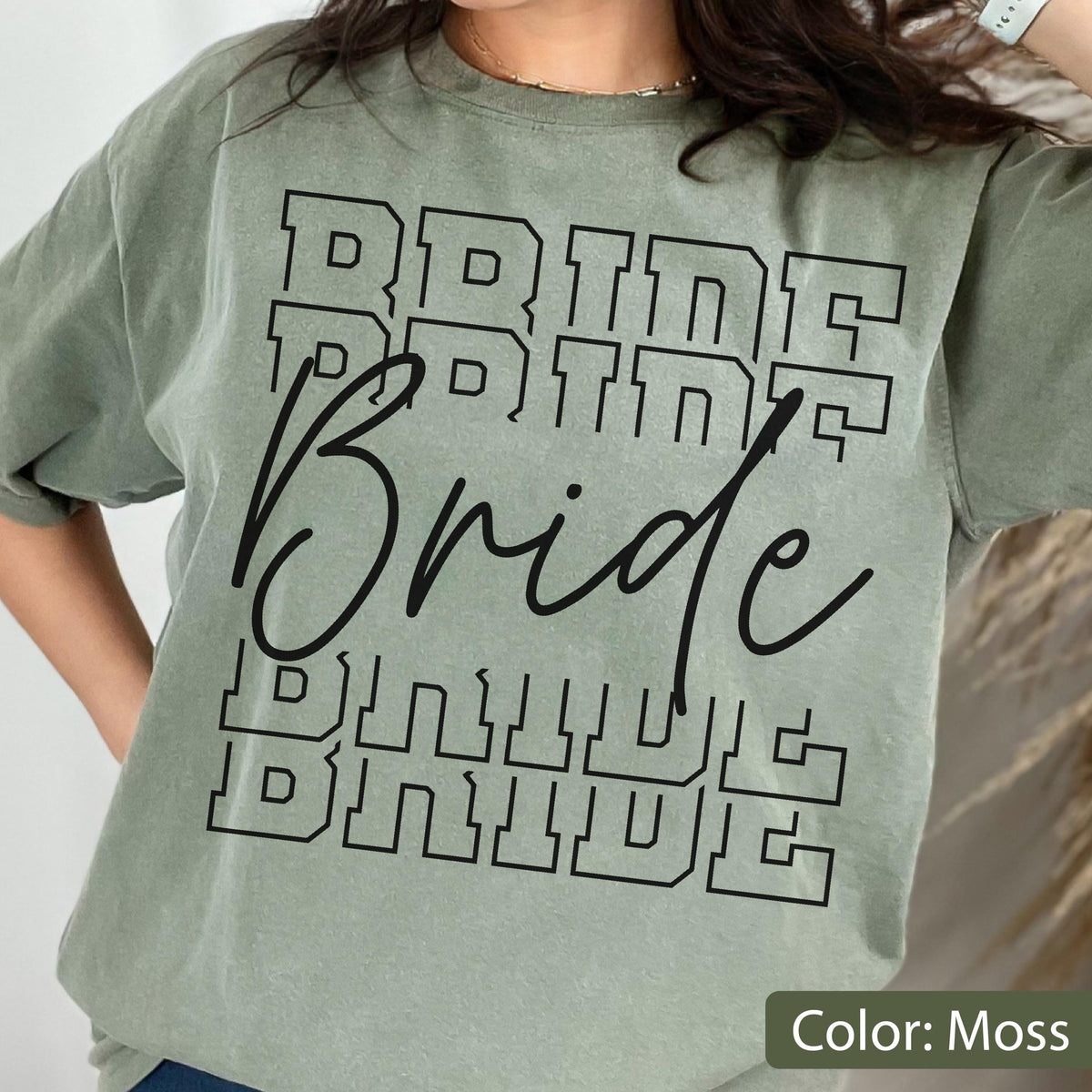 May include: A moss green t-shirt with the word "Bride" printed in a bold, black font. The word is repeated multiple times in a stacked design. The shirt has a crew neck and short sleeves.