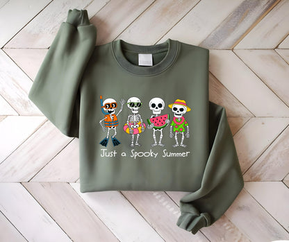 May include: Olive green sweatshirt with a graphic of four skeleton characters in summer attire. One wears a snorkel, another sunglasses, a third holds watermelon, and the last wears a straw hat. Text reads "Just a Spooky Summer."