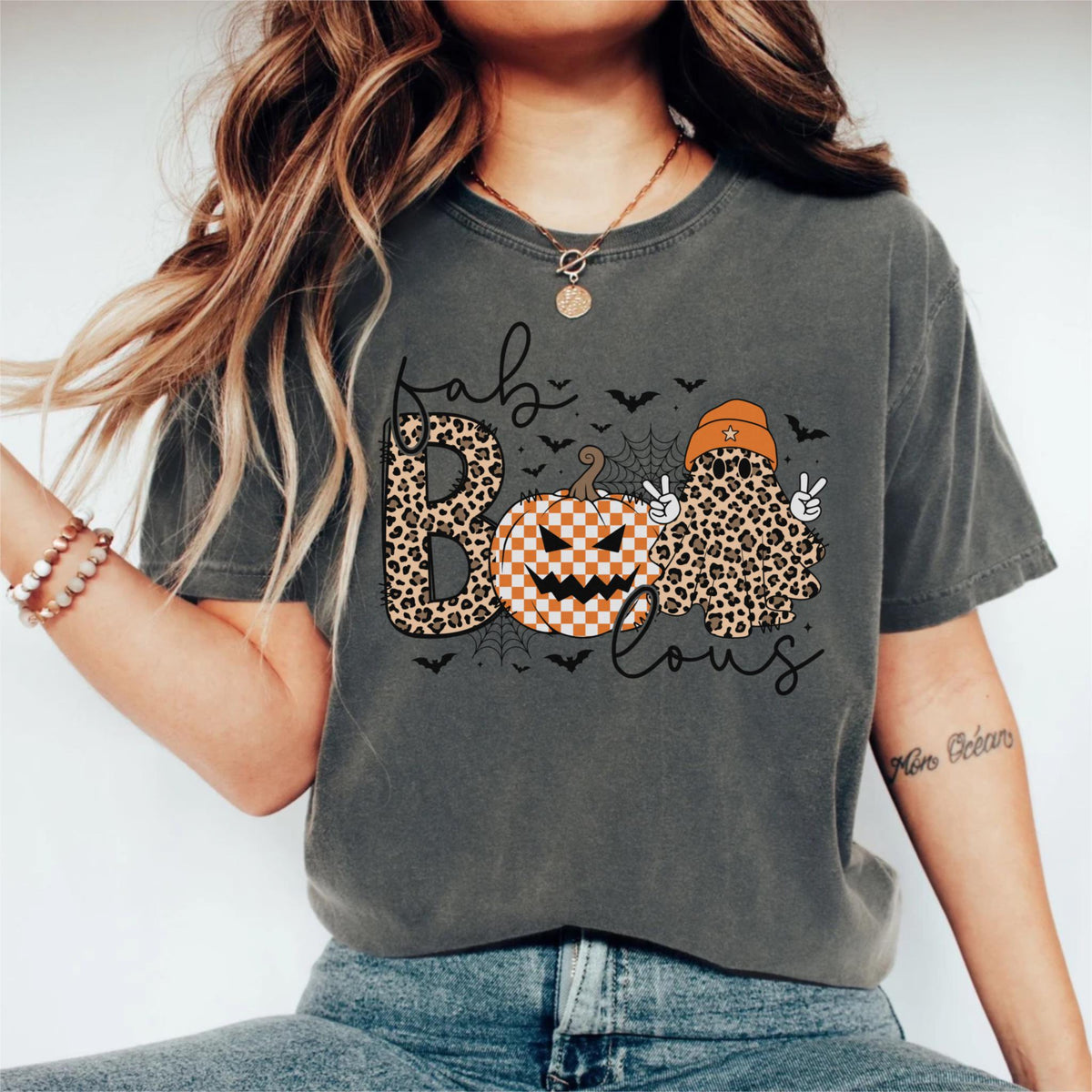 May include: A charcoal gray short-sleeve t-shirt featuring a graphic with the text "fab BOO lous". The design includes a leopard print letter B, a checkered pumpkin, a leopard print ghost wearing an orange beanie, spiderwebs, and bats.
