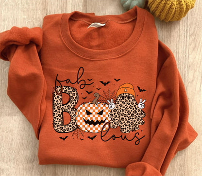 May include: An orange crewneck sweatshirt featuring a graphic with the text "fab BOO lous". The design includes a leopard print letter B, a checkered pumpkin, a ghost wearing an orange beanie, small black bats, and a spider web illustration.