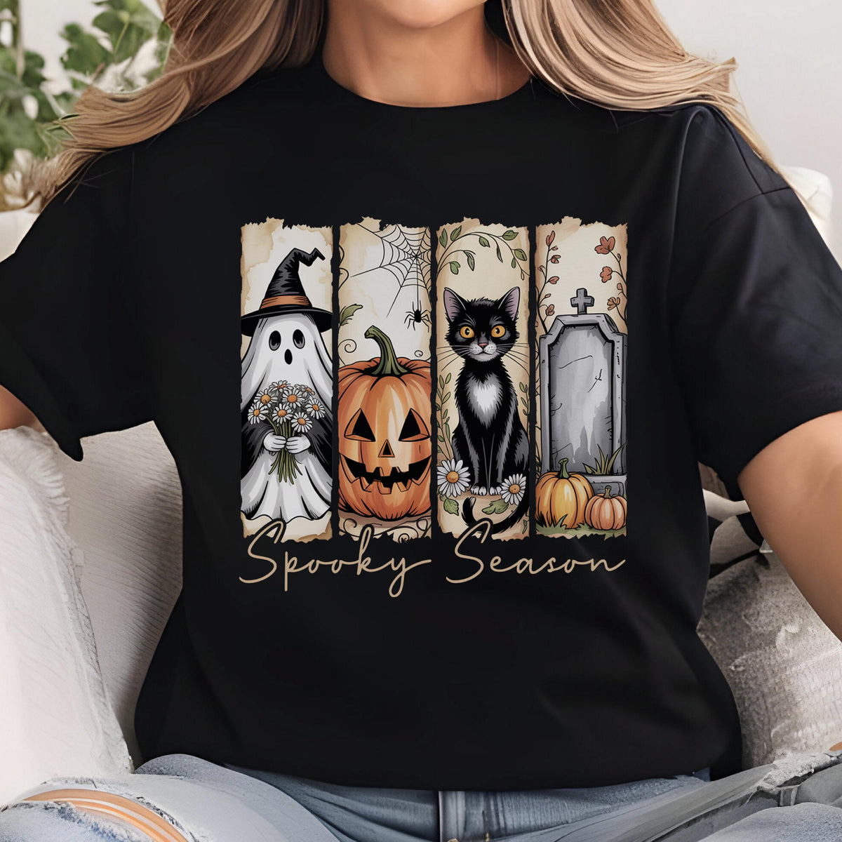 May include: A black t-shirt featuring a graphic print divided into four vertical panels. The panels display a ghost in a witch hat holding flowers, a jack-o'-lantern with a spider web, a black cat with daisies, and a tombstone. The text Spooky Season is below.