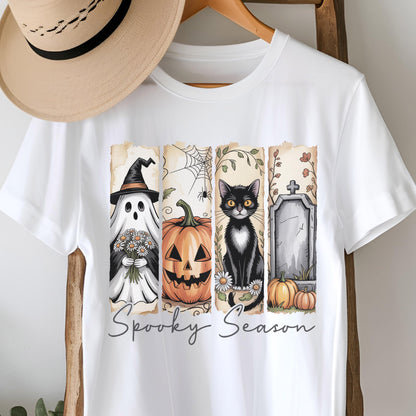 May include: A white short-sleeve t-shirt featuring a graphic print with four vertical panels depicting a ghost with flowers, a jack-o'-lantern, a black cat, and a tombstone with pumpkins. The text Spooky Season is printed below in gray.