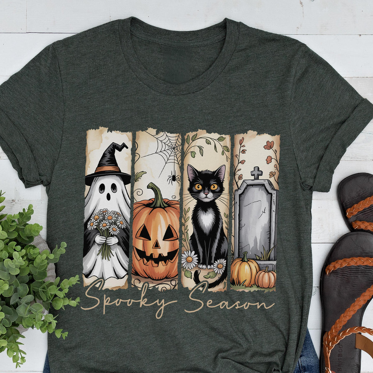 May include: A dark charcoal gray t-shirt featuring a graphic print of four vertical panels with a ghost in a witch hat, a jack-o'-lantern, a black cat, and a tombstone. The text Spooky Season is printed in a cursive font below the panels.